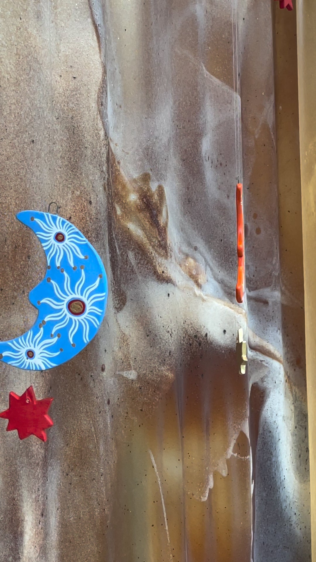 Crescent moon & star decorations hang beautifully from beauty retail store window, in bright periwinkle blue, orange & red